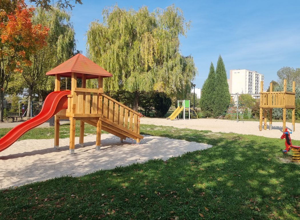 drewniana zjeżdżalnia, pod nią biały piasek i zielona trawa