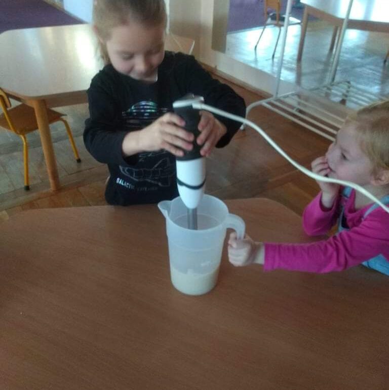 Dziewczynka trzyma blender, a druga trzyma pojemnik do blendowania