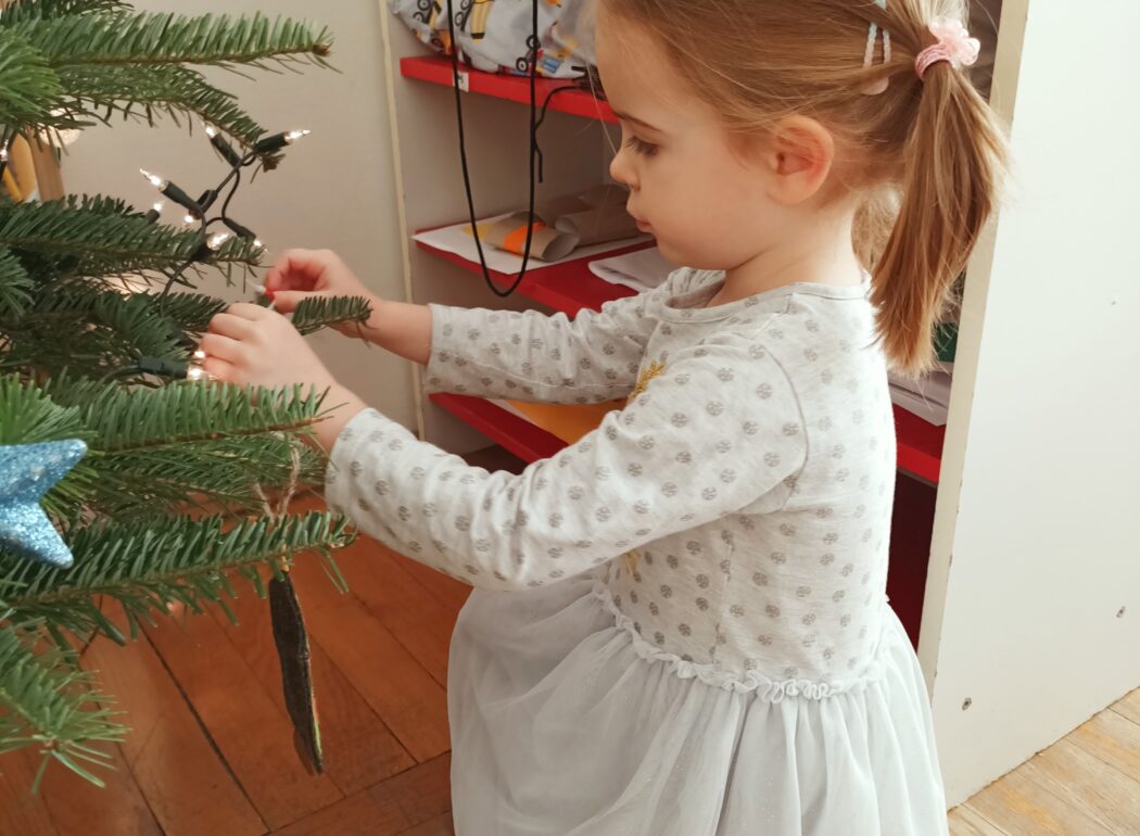 Dziewczynka w białej sukience wiesza ozdobę na choince