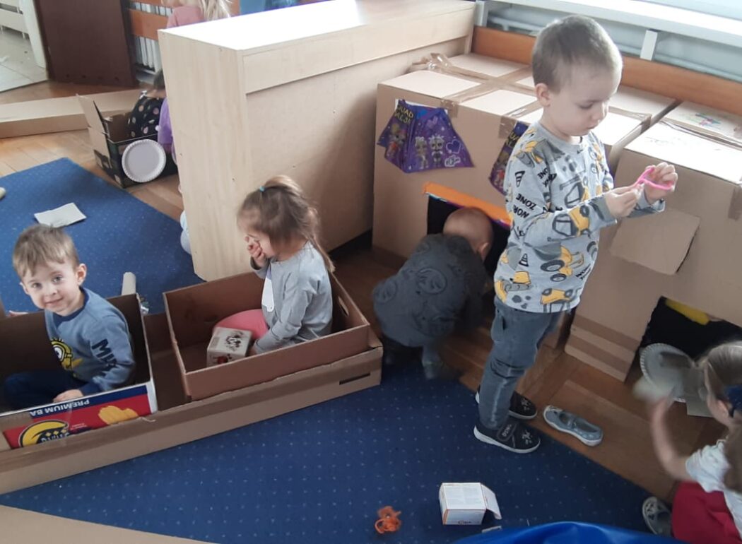 dziecko wchodzące do domu z kartonu obok dzieci w samochodzie z kartonów