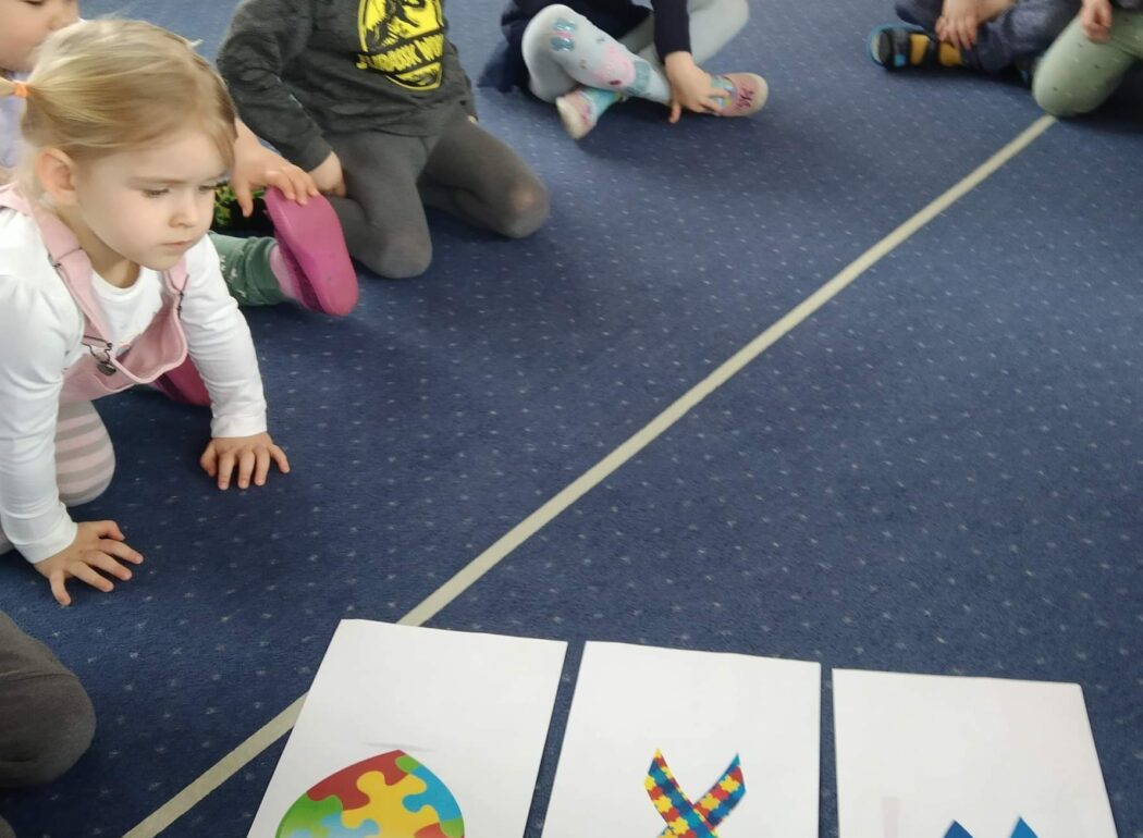 dzieci siedzą na niebieskim dywanie na którym położone są obrazki