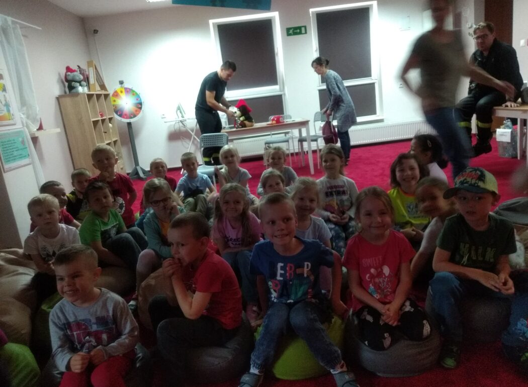 ciemna sala, dzieci siedzą na dywanie i uśmiechają się