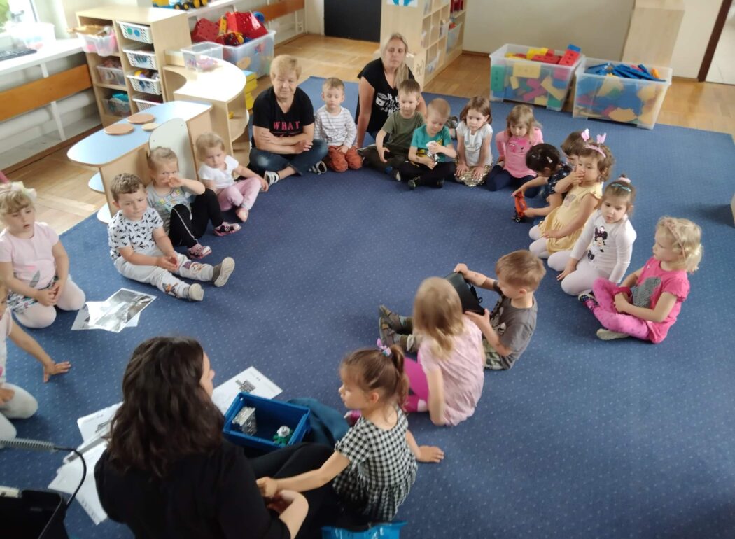 dzieci siedzą w kręgu na niebieskim dywanie
