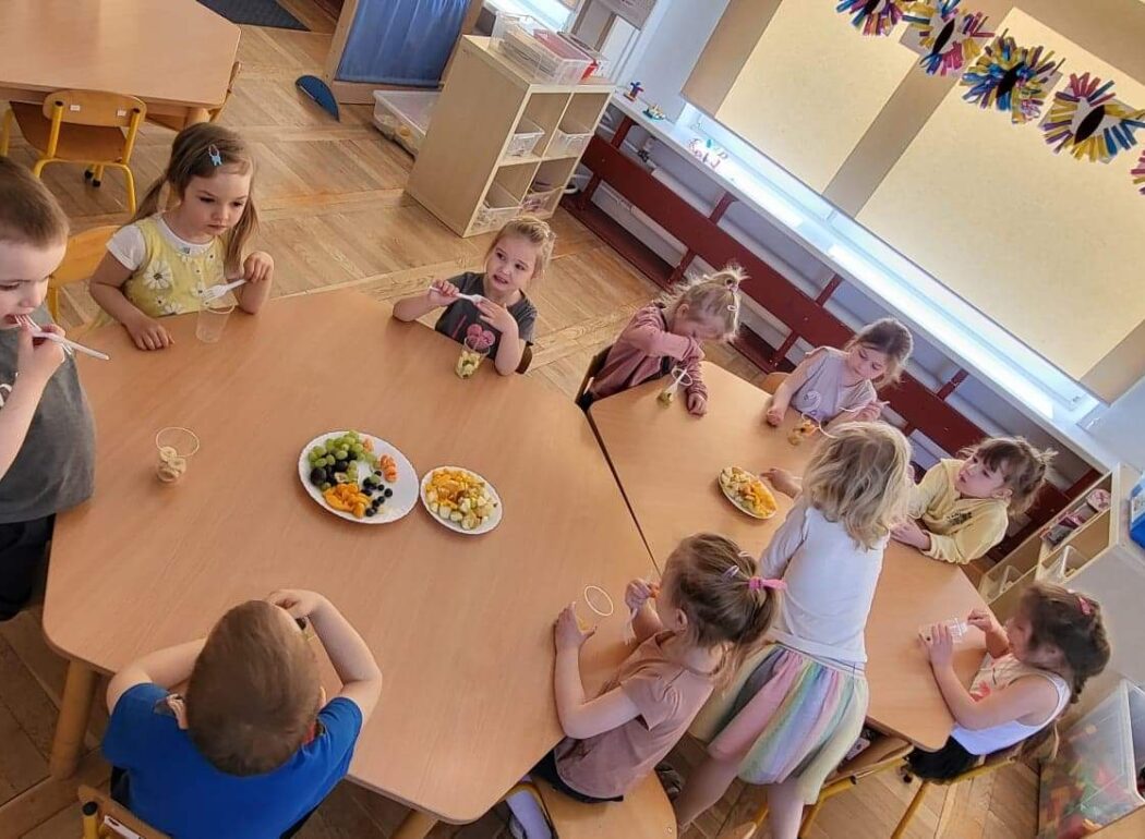 dzieci siedzą przy stole, na stole są talerze z owocami