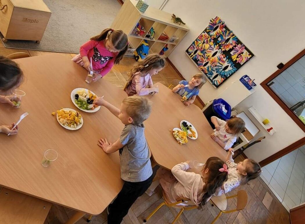 dzieci siedzą przy stole, na stole są talerze z owocami