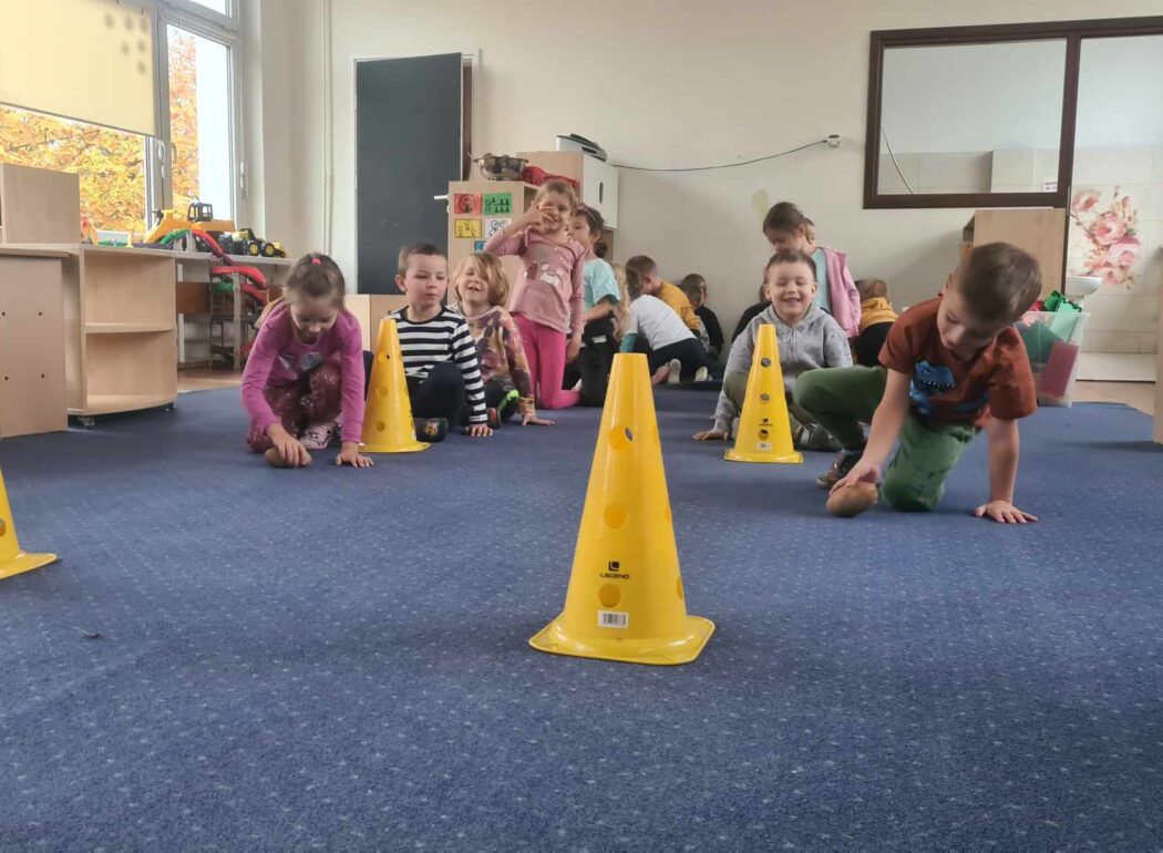 na niebieskim dywanie dzieci idą na czworakach między pachołkami