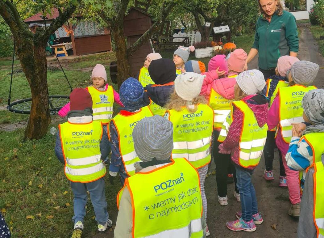 Dzieci w odblaskowych kamizelkach chodzą sród drzew