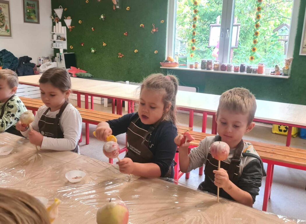 dzieci trzymają w rękach jabłka nadziane na patyczkach, dekorują je lukrem