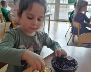 Dziewczynka wkłada żurawinę do kubeczka z musem owocowym