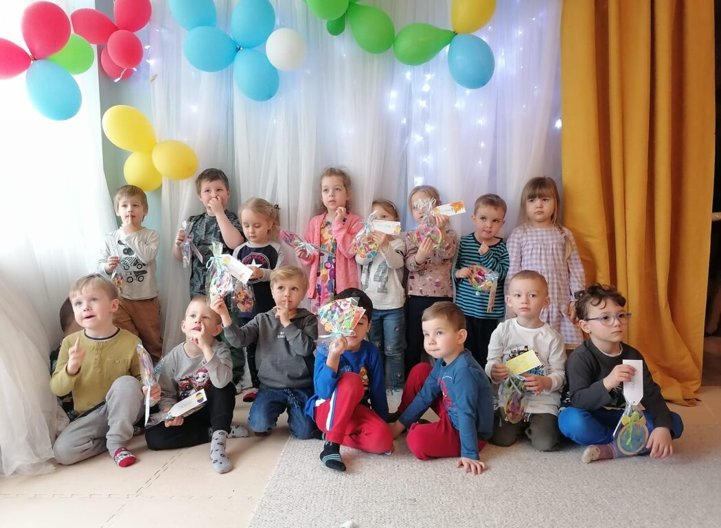 uśmiechnięte dzieci stoją na tle ściany udekorowanej balonami trzymają w rękach woreczki z celofanu z kolorową zawarością